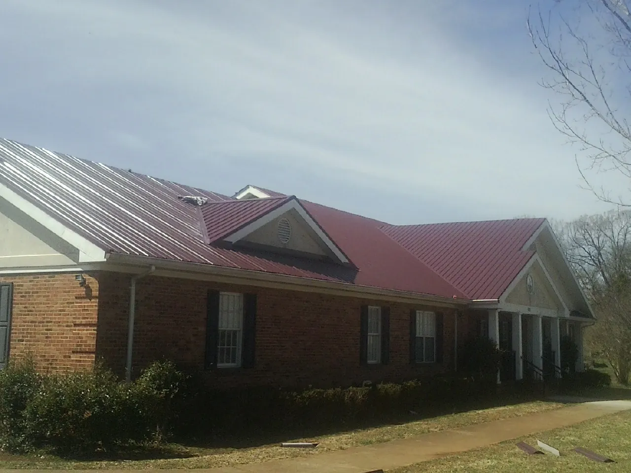 Red metal roof with gabled entries on a long brick building, from a Hail Damage Roof Repair job in Allenport