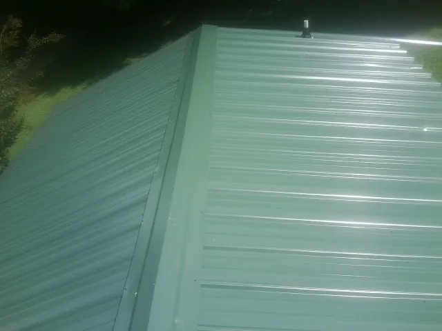 New green metal panels meeting at the ridge of a roof — Flat Roof Repair work by our crew in Allenport