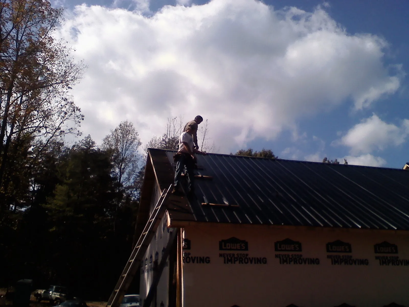 Roofer fastening dark metal panels high against a cloudy sky, from a Roof Inspection job in Allenport
