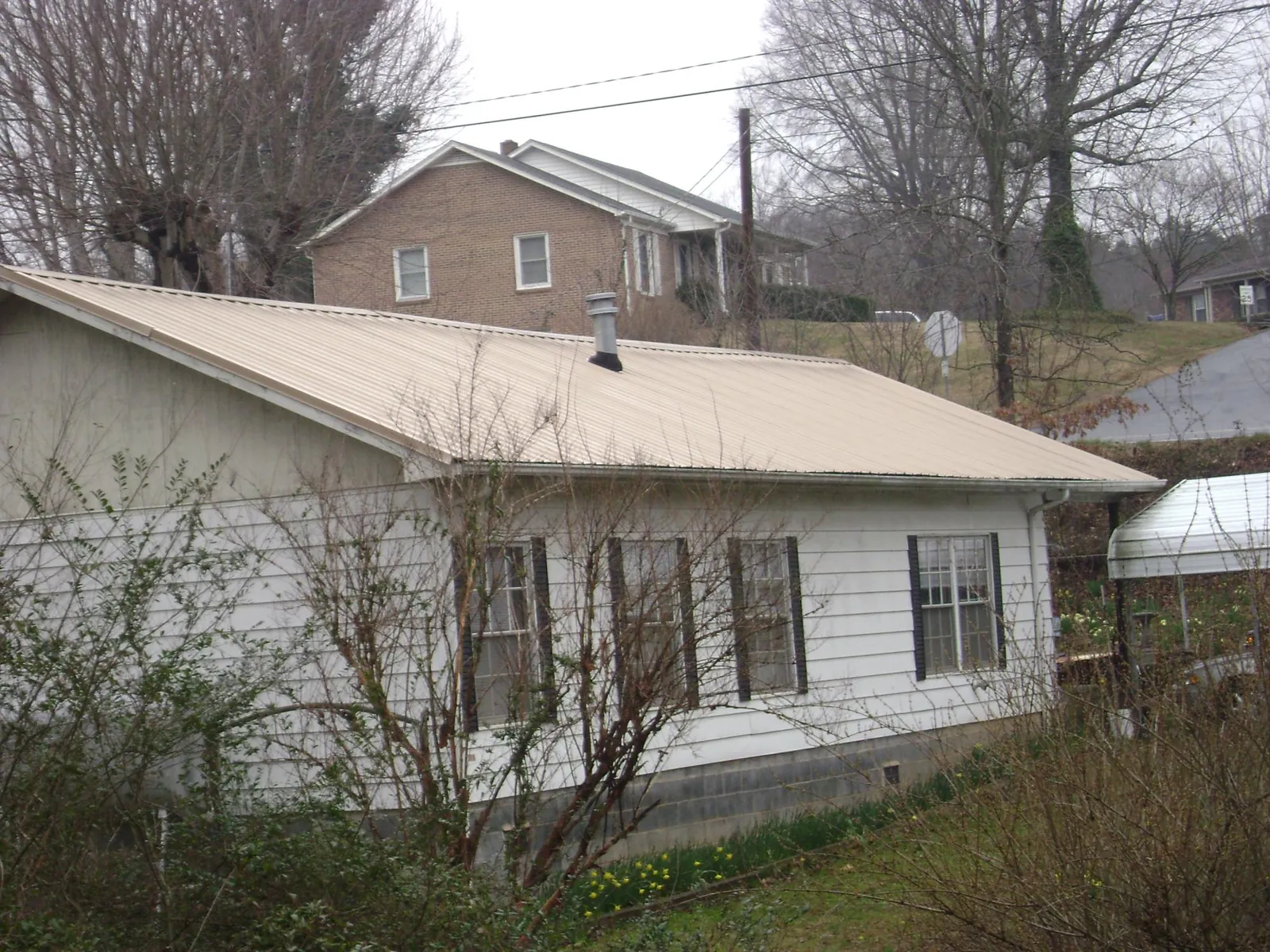 Tan metal roof on a white sided house set into a hillside — Commercial Roofing by Roofing Brothers in Allenport